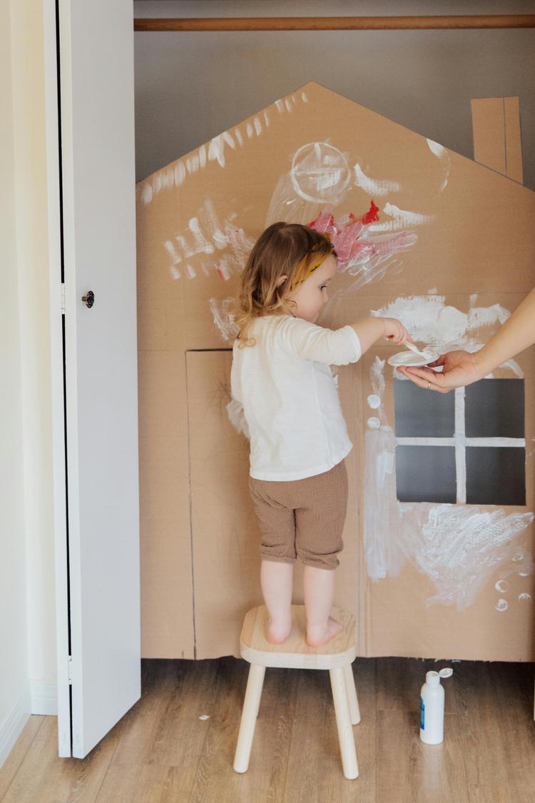 Une fillette peinture une maison en carton