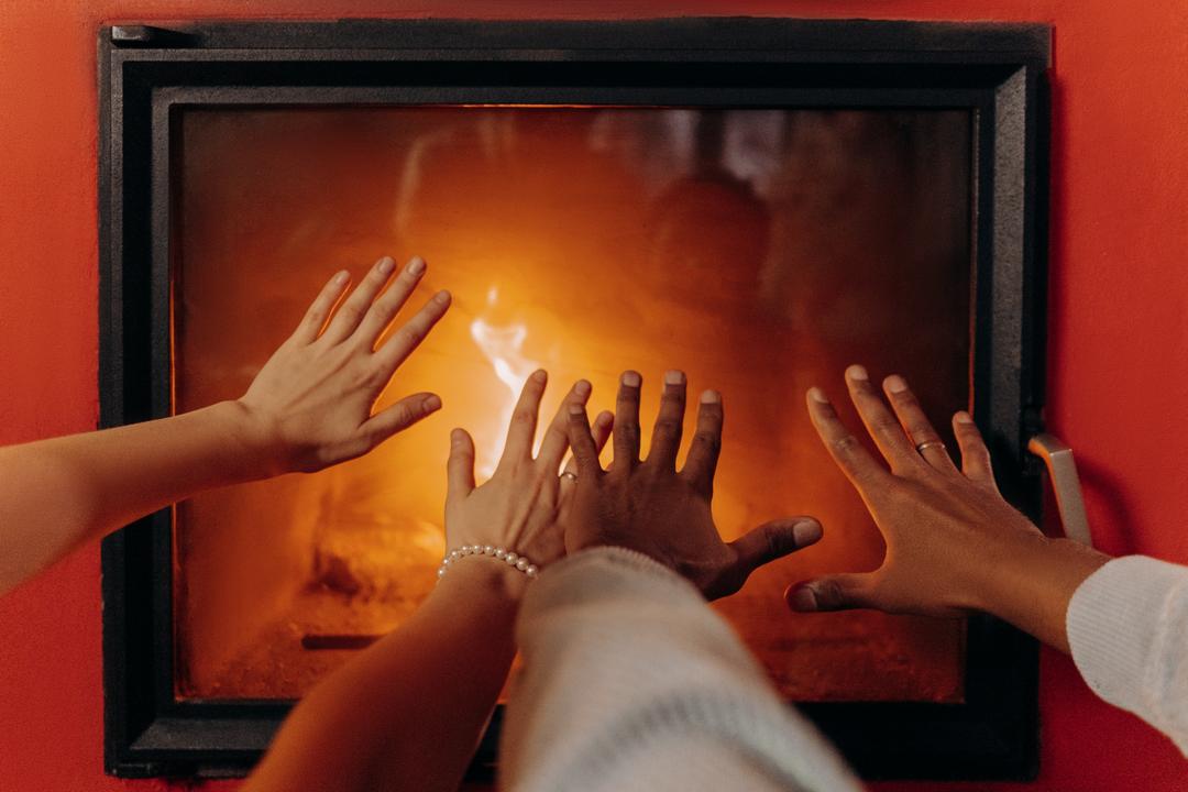 Couple se réchauffant les mains devant le foyer à bois de leur maison