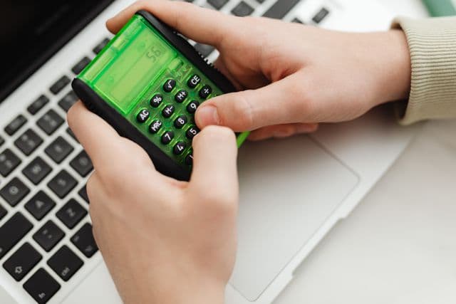 Personne qui utilise une calculatrice devant un ordinateur portable