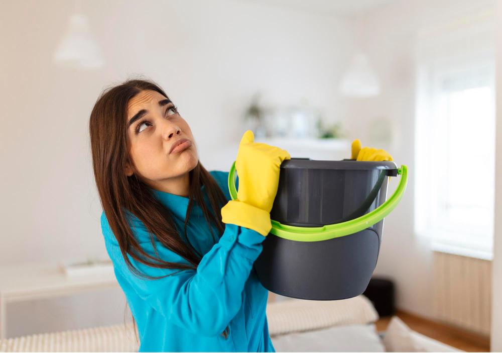 Femme récoltant l’eau fuyant du plafond avec un sceau