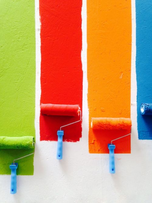 Rouleaux faisant des traits de peinture vert, rouge orange et bleu sur un mur