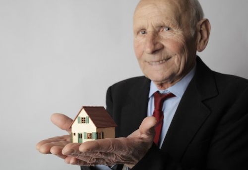 Vieil homme tenant une petite maison entre ses mains